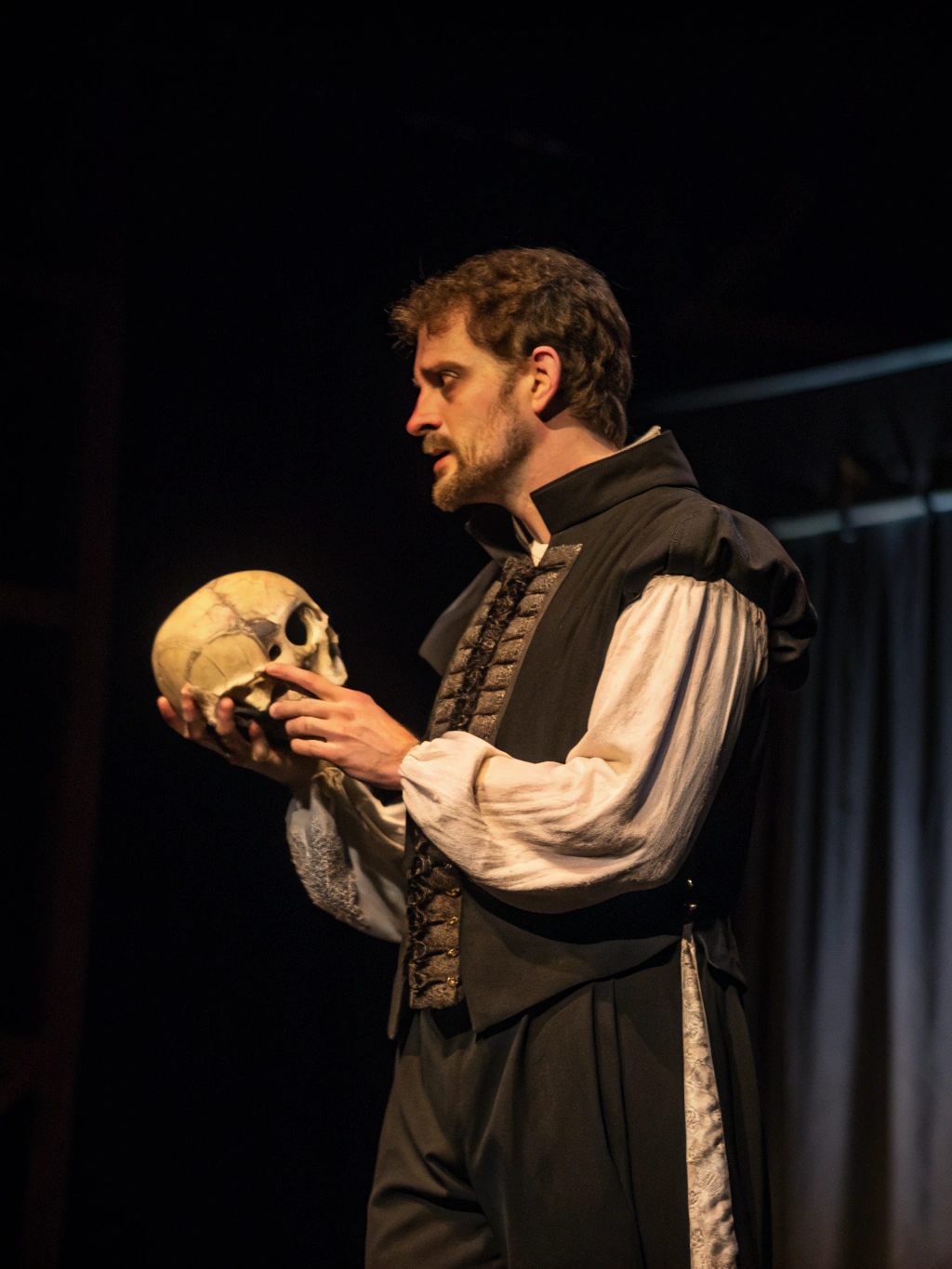 Jordan Rivers as Hamlet — high-contrast dramatic stage lighting with silver accents